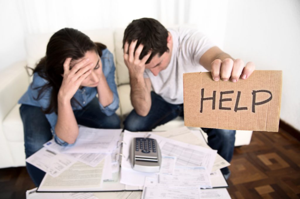 young couple worried in need of money asking for help in cardboard text message sitting in stress at home living room couch accounting debt bills bank , documents , receipts and payments feeling desperate in bad financial situation